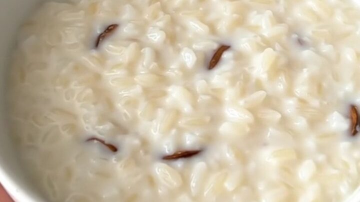 A close overhead view of creamy vanilla rice pudding inside a black slow cooker on a white quartz countertop.