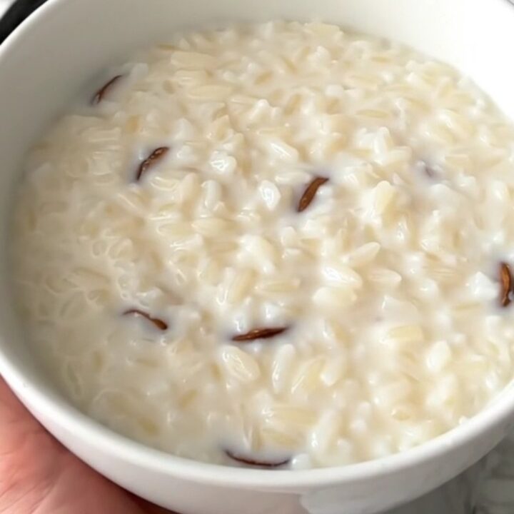 A close overhead view of creamy vanilla rice pudding inside a black slow cooker on a white quartz countertop.