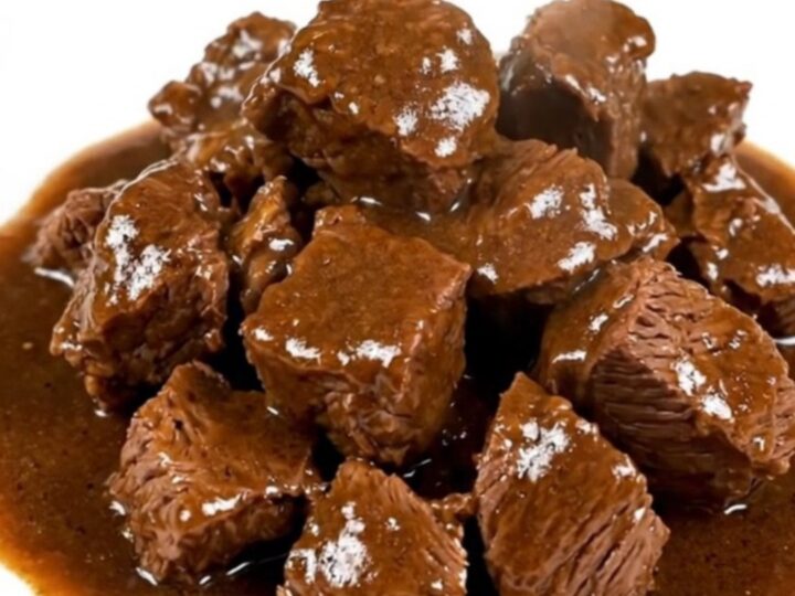 A close-up of a steaming bowl of Flemish carbonnade with tender beef chunks in a rich, dark glossy gravy.