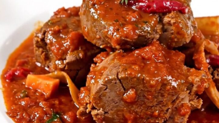 A close-up of a slow cooker filled with veal shanks, diced carrots, celery, and a rich tomato sauce.