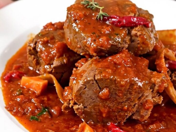 A close-up of a slow cooker filled with veal shanks, diced carrots, celery, and a rich tomato sauce.