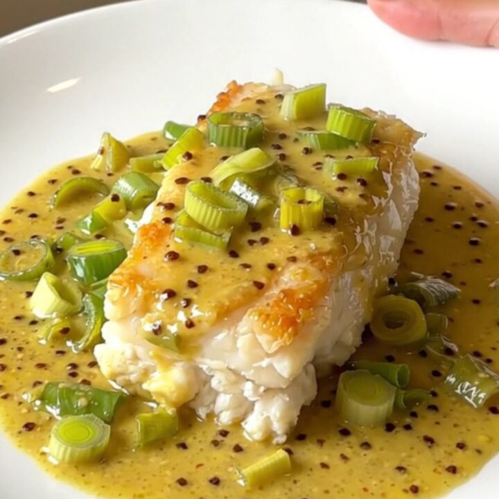 A slow cooker filled with cod loins, sliced leeks, and a creamy mustard sauce.