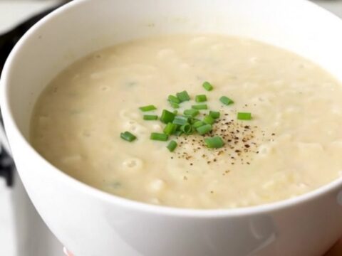 A bowl of smooth, creamy potato leek soup garnished with fresh herbs, held by a hand against a kitchen background.