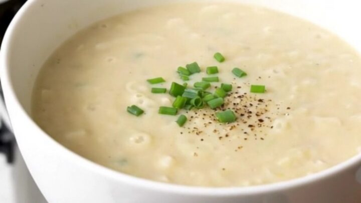 A bowl of smooth, creamy potato leek soup garnished with fresh herbs, held by a hand against a kitchen background.