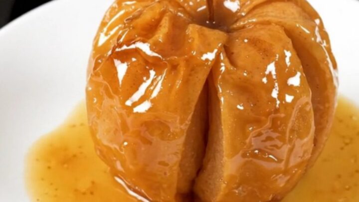 A close-up of a warm, glossy baked apple with cinnamon and brown sugar, served on a white plate.