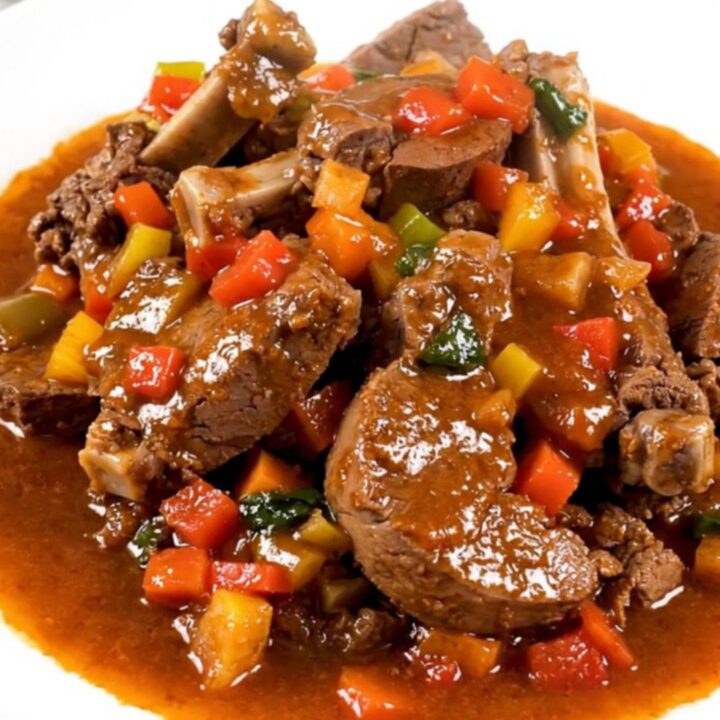 A top-down view of raw veal cubes, sliced carrots, and mushrooms inside a black oval slow cooker on a white quartz