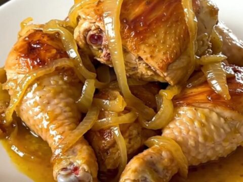 A close-up of a slow cooker filled with chicken legs, sliced onions, and a glossy lemon-mustard sauce.