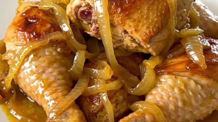 A close-up of a slow cooker filled with chicken legs, sliced onions, and a glossy lemon-mustard sauce.