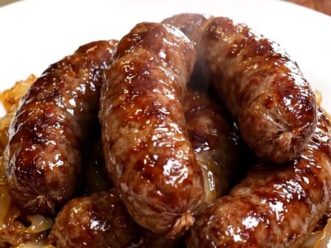 A rustic plate featuring golden-brown diots de savoie sausages topped with softened onions in a white wine sauce.