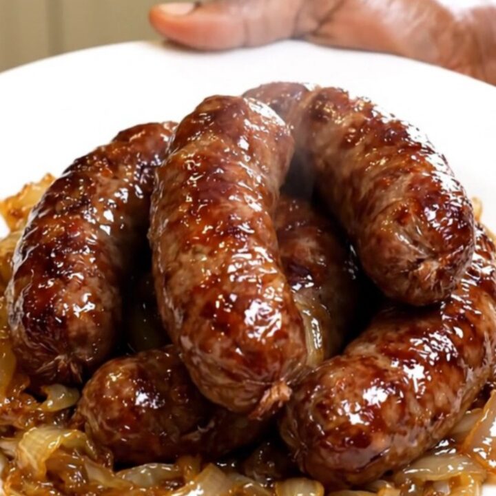 A rustic plate featuring golden-brown diots de savoie sausages topped with softened onions in a white wine sauce.