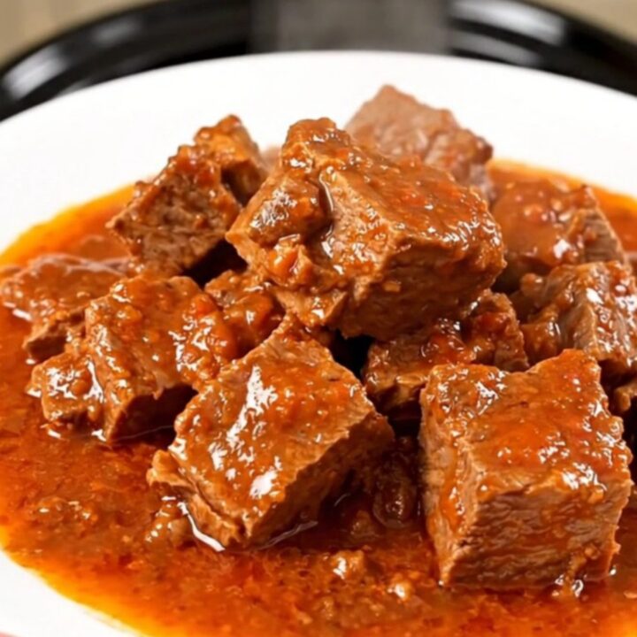 A close-up of a slow-cooker Provençal pork stew served on a white plate with visible chunks of tender pork and peppers.