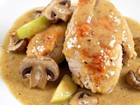 A close-up of slow cooker Normandy chicken served on a white plate with visible apple slices and mushrooms.