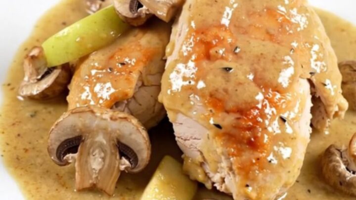 A close-up of slow cooker Normandy chicken served on a white plate with visible apple slices and mushrooms.