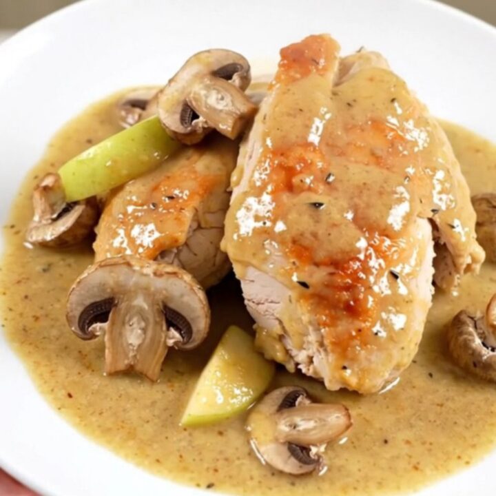 A close-up of slow cooker Normandy chicken served on a white plate with visible apple slices and mushrooms.