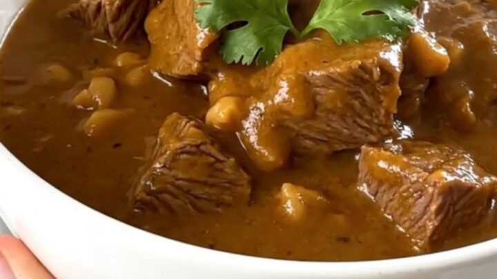 A steaming bowl of beef peanut stew with tender beef cubes and sweet potatoes in a rich sauce.