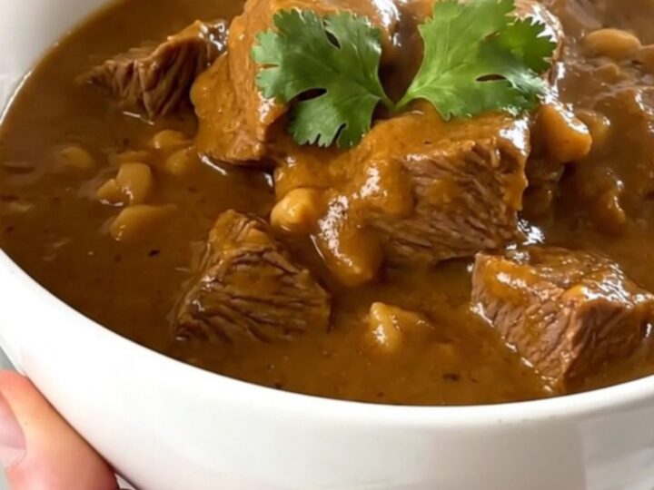 A steaming bowl of beef peanut stew with tender beef cubes and sweet potatoes in a rich sauce.