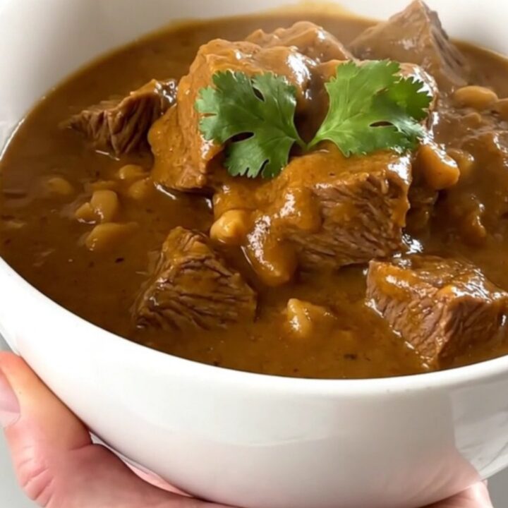 A steaming bowl of beef peanut stew with tender beef cubes and sweet potatoes in a rich sauce.
