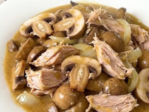 A top-down view of a slow cooker filled with raw turkey, mushrooms, and onions.