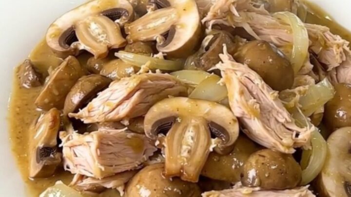 A top-down view of a slow cooker filled with raw turkey, mushrooms, and onions.