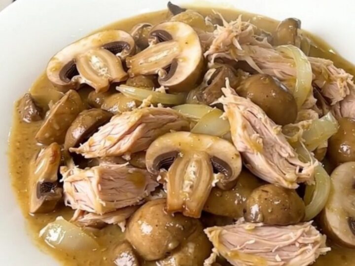 A top-down view of a slow cooker filled with raw turkey, mushrooms, and onions.