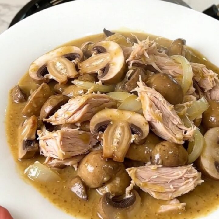 A top-down view of a slow cooker filled with raw turkey, mushrooms, and onions.