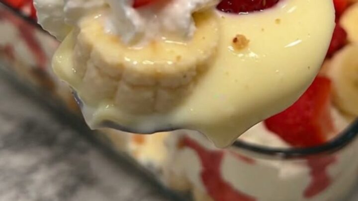 A clear glass dish filled with layers of vanilla pudding, sliced bananas, strawberries, and vanilla wafers.