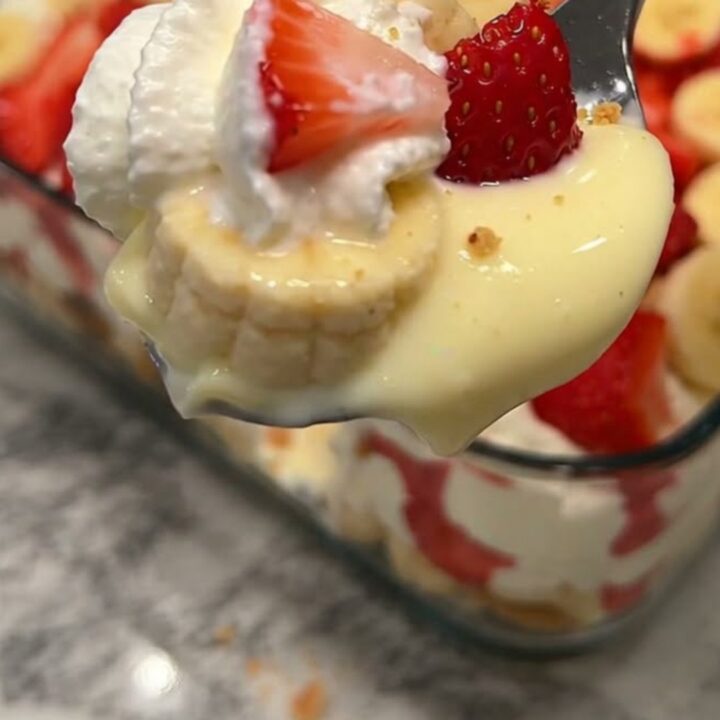 A clear glass dish filled with layers of vanilla pudding, sliced bananas, strawberries, and vanilla wafers.