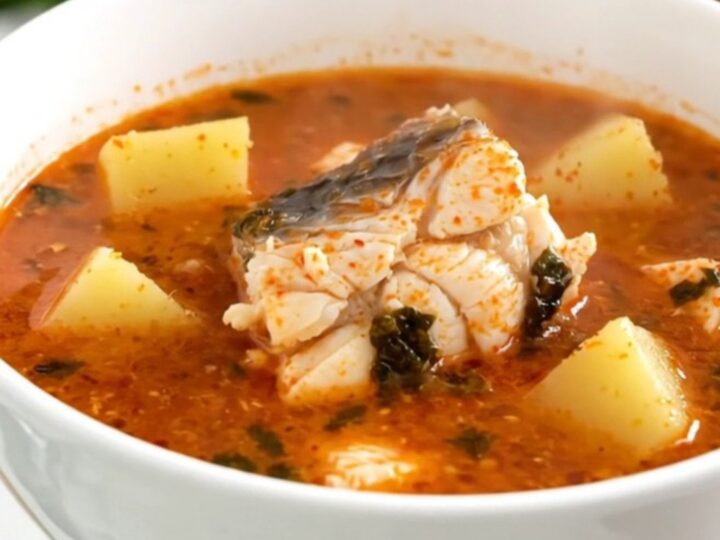 A top-down view of a black slow cooker filled with white fish, sliced potatoes, and a rich tomato broth.