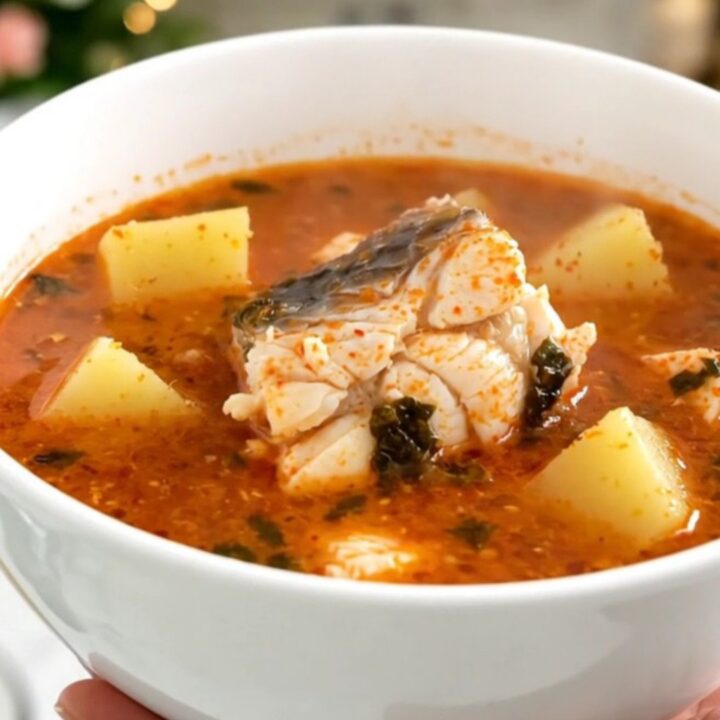 A top-down view of a black slow cooker filled with white fish, sliced potatoes, and a rich tomato broth.