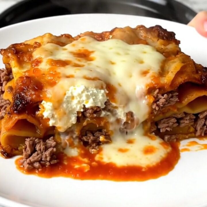 A steaming, golden slice of slow cooker beef lasagna on a white plate.