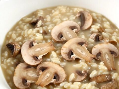 A top-down view of a black slow cooker filled with creamy mushroom risotto on a white speckled countertop.