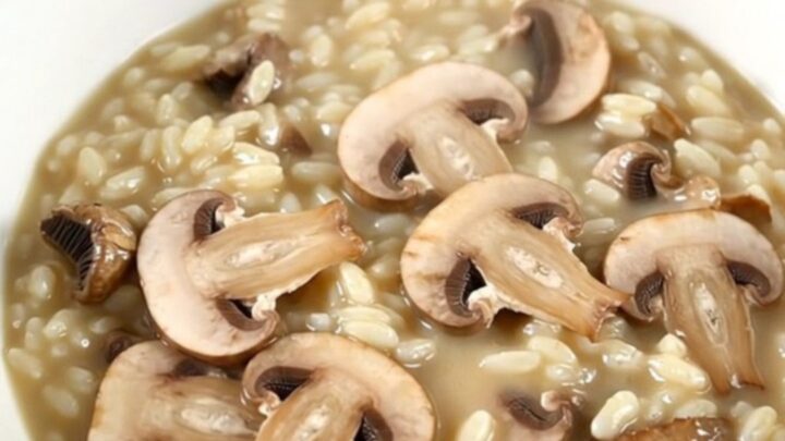 A top-down view of a black slow cooker filled with creamy mushroom risotto on a white speckled countertop.