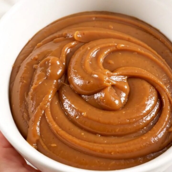 A white bowl filled with glossy, smooth vanilla chestnut spread set against a soft, blurred kitchen background.
