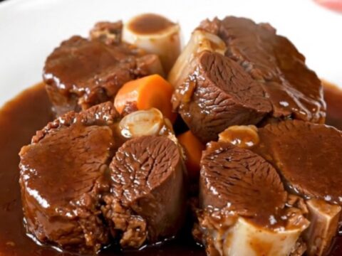 A plate of tender, glossy slow-cooked beef cheeks with carrots in a rich red wine sauce.