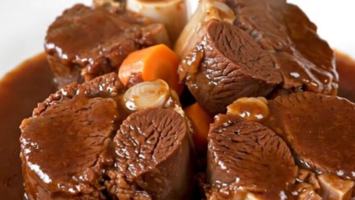 A plate of tender, glossy slow-cooked beef cheeks with carrots in a rich red wine sauce.