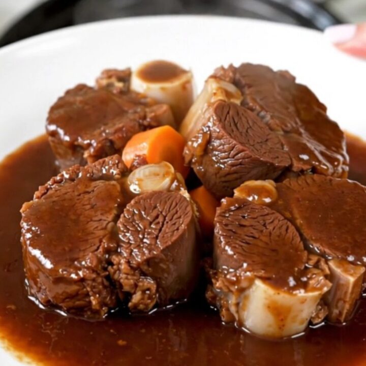 A plate of tender, glossy slow-cooked beef cheeks with carrots in a rich red wine sauce.