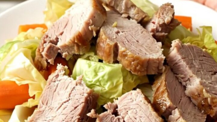 A slow cooker filled with tender salted pork, cabbage wedges, and halved carrots on a speckled quartz countertop.
