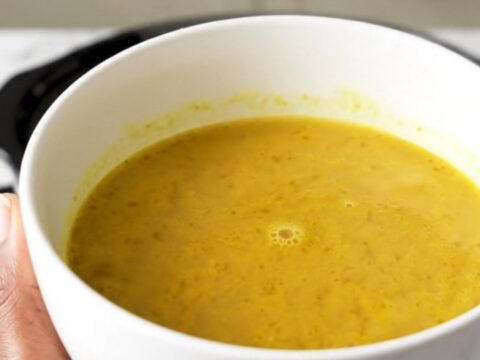A bowl of golden, velvety butternut squash coconut curry soup in a white bowl.