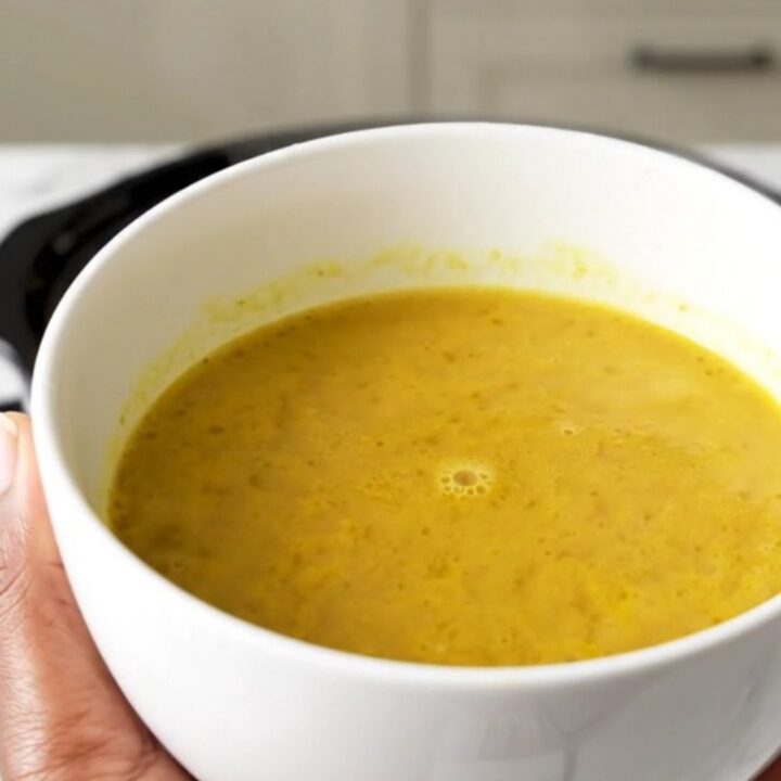 A bowl of golden, velvety butternut squash coconut curry soup in a white bowl.