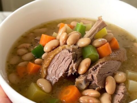 A rustic bowl of duck and bean garbure steaming on a table.