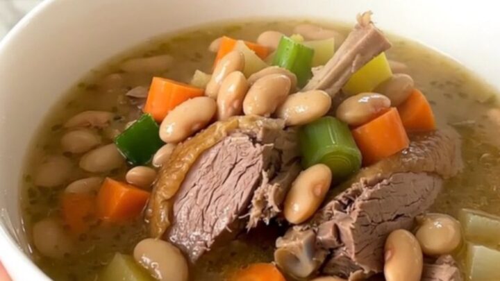 A rustic bowl of duck and bean garbure steaming on a table.