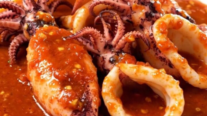 A white plate holding tender squid rings in a rich, vibrant red tomato sauce.