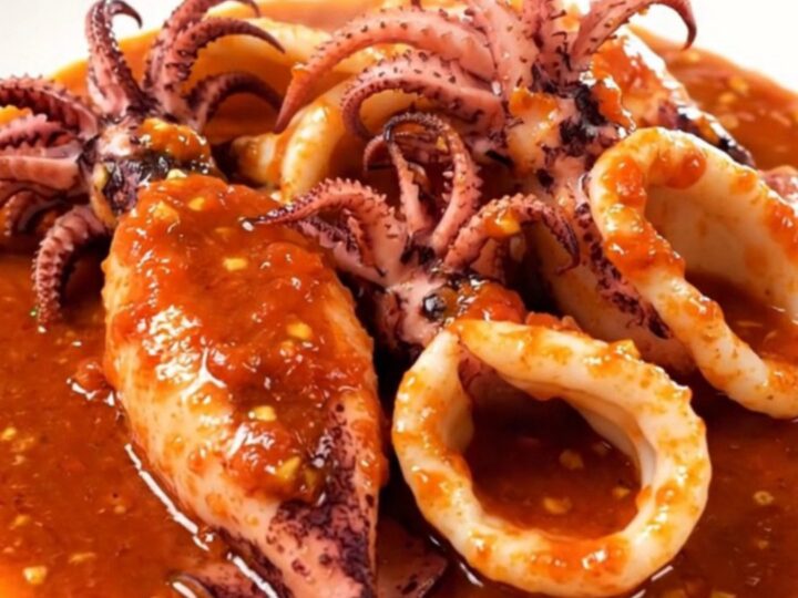 A white plate holding tender squid rings in a rich, vibrant red tomato sauce.