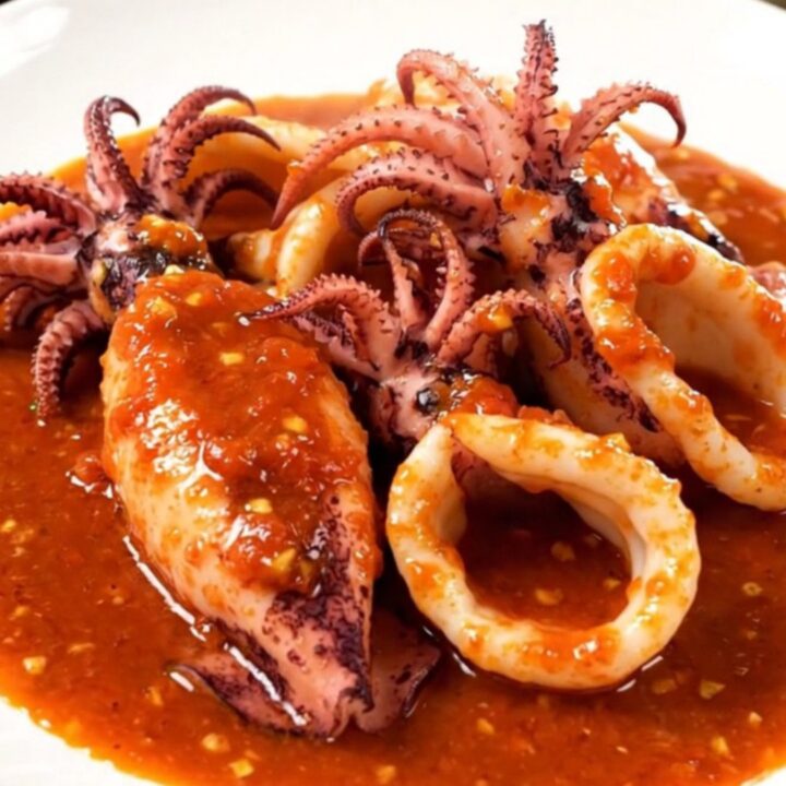 A white plate holding tender squid rings in a rich, vibrant red tomato sauce.