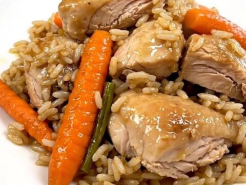 A top-down view of raw chicken, sliced carrots, and rice inside a black slow cooker on a white countertop.