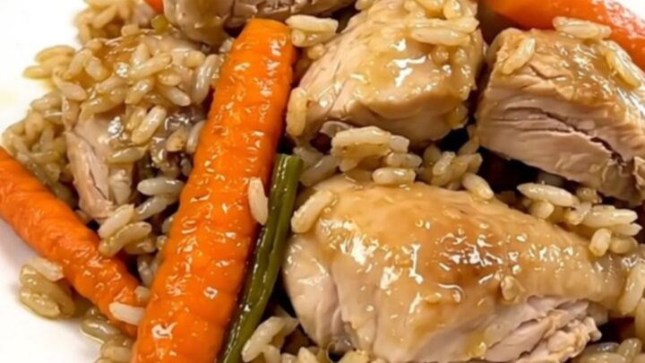 A top-down view of raw chicken, sliced carrots, and rice inside a black slow cooker on a white countertop.