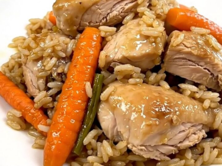A top-down view of raw chicken, sliced carrots, and rice inside a black slow cooker on a white countertop.
