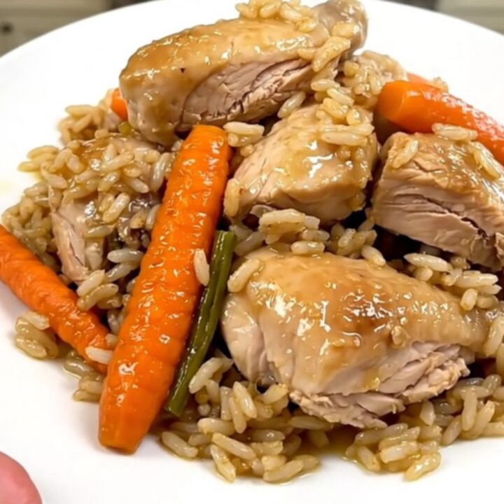 A top-down view of raw chicken, sliced carrots, and rice inside a black slow cooker on a white countertop.