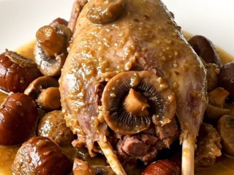 A slow cooker filled with guinea fowl, mushrooms, and chestnuts in a savory wine sauce on a white quartz countertop.