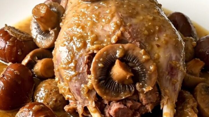 A slow cooker filled with guinea fowl, mushrooms, and chestnuts in a savory wine sauce on a white quartz countertop.
